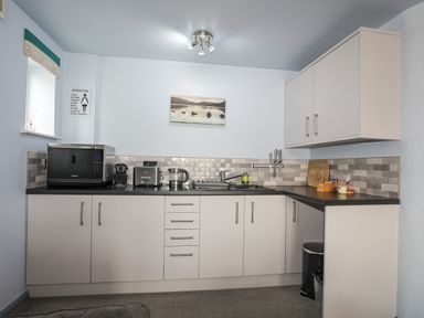A kitchen with white cabinets a microwave toaster kettle knives and a sink at Tegid Lakeside - Bala Lake in Bala