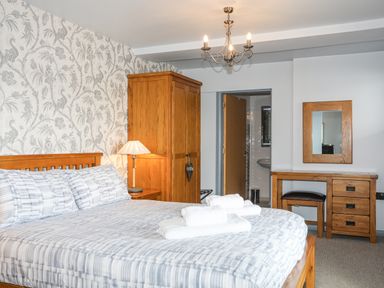 A bedroom with a double bed with towels on it a wooden wardrobe a bedside table with a lamp a dressing table with a mirror and stool at Tegid Lakeside - Bala Lake Bala