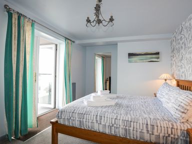 A bedroom with a wooden bed with folded towels on the bed next to a window with teal and cream curtains at Tegid Lakeside - Bala Lake in Bala