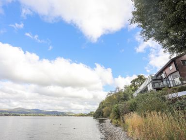A lakeside view with a house on the right and trees along the shore at Tegid Lakeside - Bala Lake in Bala