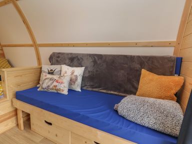 A wooden framed blue cushioned bench with animal print pillows and folded blankets at Mischief in Little Kelk near Bridlington