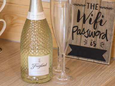 A bottle of Freixenet Prosecco with two empty champagne glasses and a wooden sign showing WiFi password area