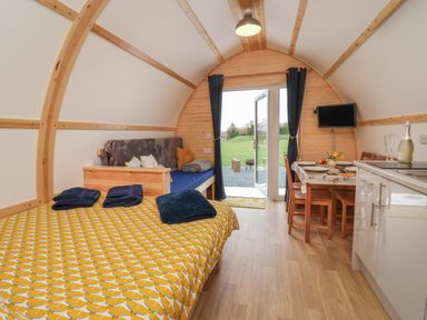 A wooden pod interior with a bed, sofa, dining table, kitchenette, and glass door opening to a garden at Mischief in Little Kelk near Bridlington