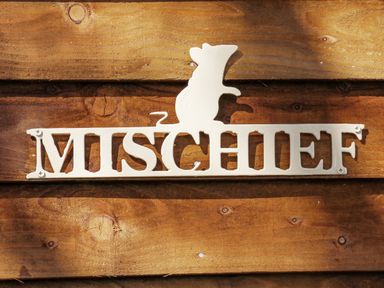 A white metal sign with the word mischief and a mouse figure mounted on a wooden surface at Mischief in Little Kelk near Bridlington