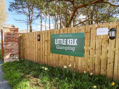 A wooden fence with a sign that reads welcome to Little Kelk Glamping and daffodils in front of the fence at Mischief in Little Kelk near Bridlington