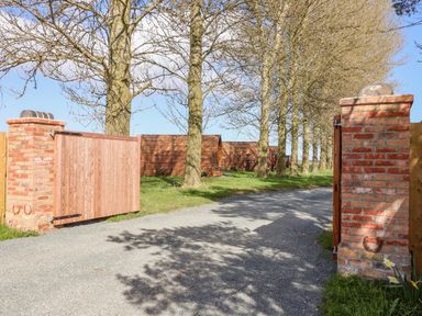 A gated driveway with wooden gates and brick pillars leading to wooden cabins and trees at Mischief Little Kelk near Bridlington