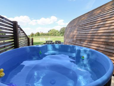 An outdoor hot tub with rubber ducks near a wooden fence and building with picnic tables and green field in the background at Mischief in Little Kelk near Bridlington
