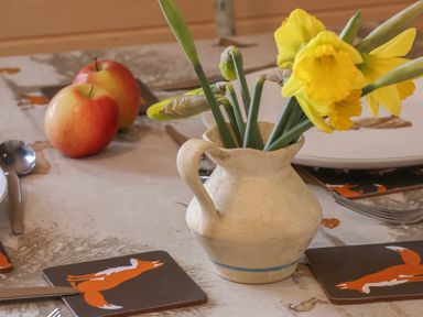 A table with a ceramic jug holding yellow flowers two apples and coasters with fox illustrations at Covey in Little Kelk near Bridlington