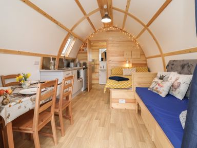 A small wooden cabin interior with a dining table and chairs kitchen area bed and sofa with cushions at Covey in Little Kelk near Bridlington