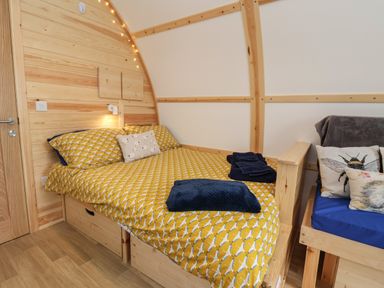 A bedroom with a wooden bed with yellow patterned bedding and a small seating area with cushions at Covey in Little Kelk near Bridlington