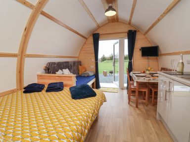 An interior of a wooden cabin with a bed, sofa, dining table, kitchen area and open door leading outside at Covey in Little Kelk near Bridlington
