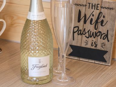 A bottle of Freixenet prosecco with two empty champagne flutes and a wooden sign with wifi password information at Covey in Little Kelk near Bridlington