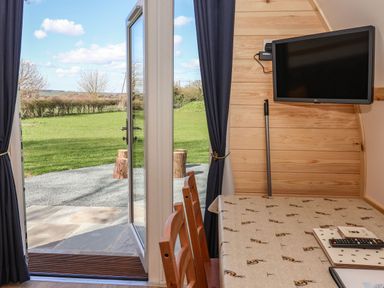 A dining area with wooden chairs and a table near an open glass door with a TV mounted on a wooden wall at Covey in Little Kelk near Bridlington
