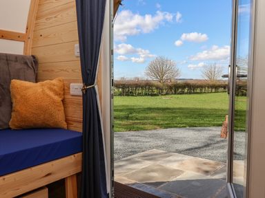 An open door leading to a garden with grass trees and hedges viewed from a room with a wooden bench blue cushion and yellow pillow at Covey in Little Kelk near Bridlington
