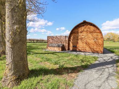 A wooden pod with a gravel path and a tree in a grassy field at Covey Little Kelk near Bridlington
