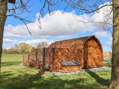 A wooden pod with a fenced area in a grassy field with trees and blue sky at Covey in Little Kelk near Bridlington
