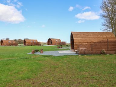 A grassy field with four wooden curved cabins and outdoor seating at Covey in Little Kelk near Bridlington