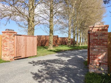 An open wooden gate between brick pillars leading to a driveway with trees and wooden buildings at Covey Little Kelk near Bridlington