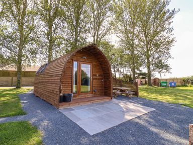A small wooden cabin with a glass door surrounded by gravel and trees at Covey in Little Kelk near Bridlington