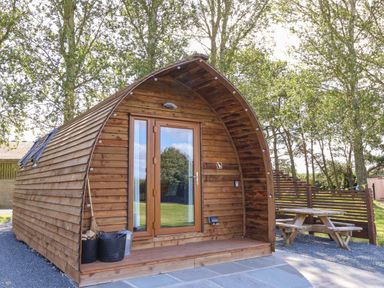 A wooden cabin with glass door and small porch beside a picnic table in a wooded area at Covey in Little Kelk near Bridlington