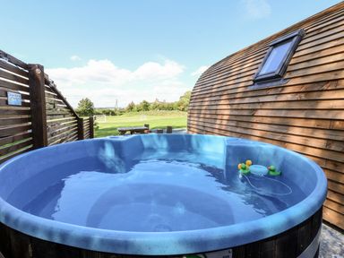 An outdoor hot tub with rubber ducks next to a wooden building and a grassy field in the background at Covey in Little Kelk near Bridlington