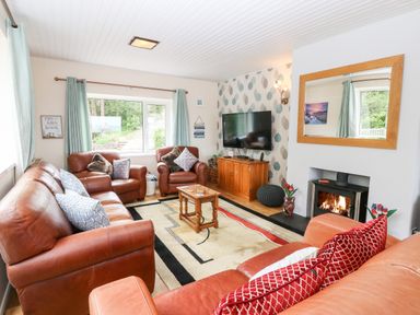A living room with leather sofas a wooden coffee table a wall-mounted television and a fireplace at Willoway in Benllech