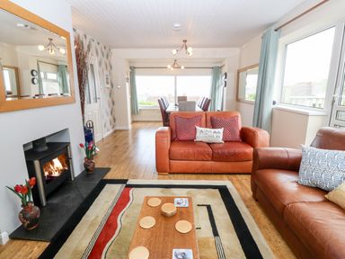 A living room with two brown leather sofas a fireplace wooden floor and a dining area at Willoway in Benllech