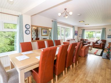 A living room with a long dining table and brown chairs next to a seating area with brown sofas at Willoway in Benllech