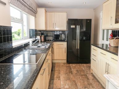 A kitchen with black countertops light wood cabinets a black double door refrigerator and a window at Willoway in Benllech