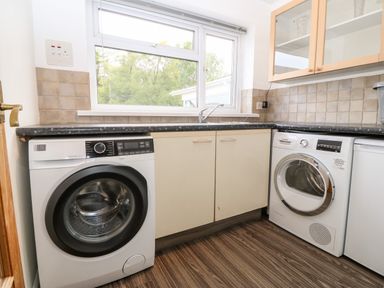 A utility room with a washing machine dryer sink and cabinets at Willoway in Benllech