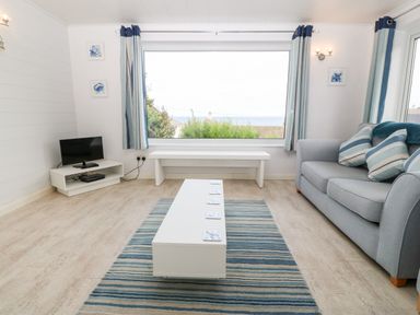 A living room with a sofa a coffee table a small television a bench and a large window with curtains at Willoway in Benllech