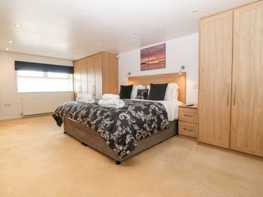A bedroom with a double bed black and white bedding wooden wardrobes and a window at Willoway in Benllech