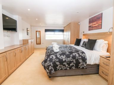 A bedroom with a double bed a mounted television wooden cabinets and a window at Willoway in Benllech