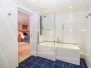 A bathroom with a bathtub and shower next to a bedroom with a bed at Willoway in Benllech