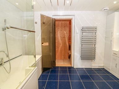 A bathroom with a bathtub shower and an open door leading to a wooden sauna at Willoway in Benllech