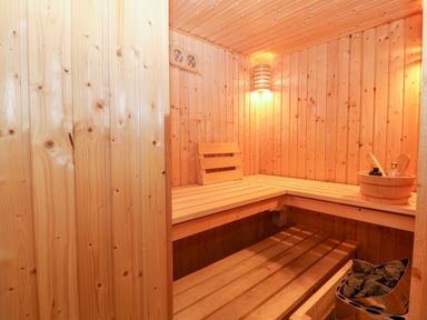 An empty wooden sauna room with benches stones in a heater and a bucket with sauna accessories at Willoway in Benllech
