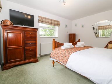 A bedroom with a wooden bed, wooden wardrobe with a TV on top, window with patterned blinds, and a large mirror on the wall at Willoway in Benllech