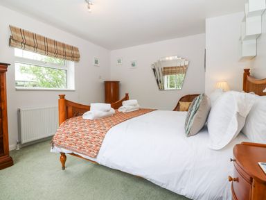 A bedroom with a wooden bed a nightstand a window and a wall mirror at Willoway in Benllech