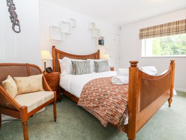 A bedroom with a wooden bed and armchair bedside tables with lamps and a window at Willoway in Benllech