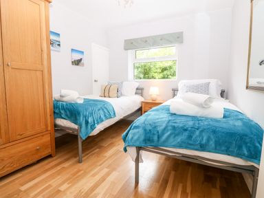 A bedroom with two single beds blue blankets wooden wardrobe and a window at Willoway in Benllech