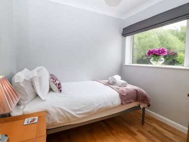 A small bedroom with a single bed a bedside table with a lamp and a window with flowers in a vase at Willoway in Benllech