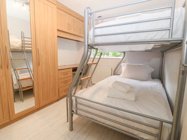 A bedroom with a bunk bed and wooden wardrobe with mirror at Willoway in Benllech