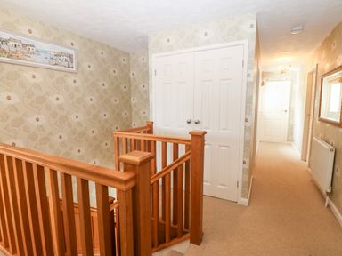 A hallway with carpeted floor wooden staircase and floral wallpaper at Willoway in Benllech