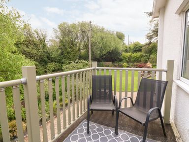 A small balcony with two black chairs and a patterned rug overlooking a garden with trees at Willoway in Benllech