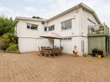 A patio area with outdoor dining table and chairs under an umbrella beside a white building with windows and a small balcony at Willoway in Benllech
