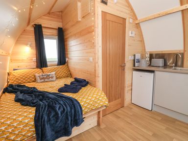 A small wooden room with a bed and yellow bedding next to a kitchenette with a mini fridge and sink at Bouquet in Little Kelk near Bridlington