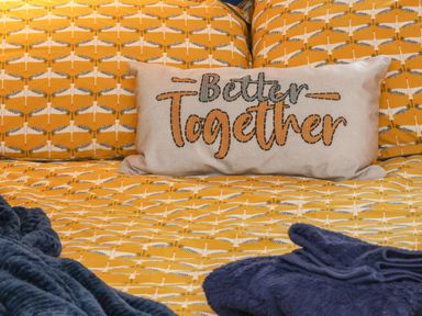 A bed with yellow patterned bedding a pillow with better together text and dark blue towels