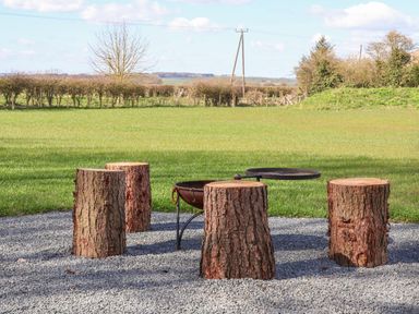 An outdoor area with four tree stump seats around a metal fire pit on a gravel surface at Bouquet in Little Kelk near Bridlington