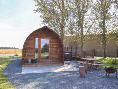A wooden pod with glass doors next to a picnic table and fire pit in an outdoor area at Bouquet in Little Kelk near Bridlington