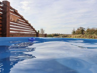 An outdoor hot tub with water and a wooden fence with a sign in a rural area at Bouquet in Little Kelk near Bridlington